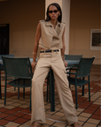 Woman Wearing Sola Trench Vest and pants standing in an outdoor setting with chairs and a table.