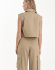 Woman wearing a beige Sola Trench Vest sleeveless top and cargo pants on a white background