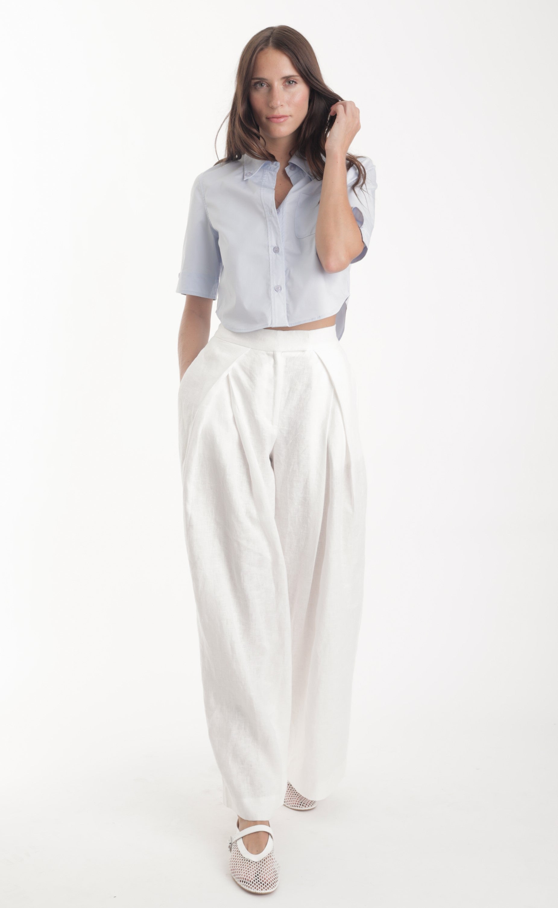 Woman wearing a light blue button-up shirt and white pants on a white background
