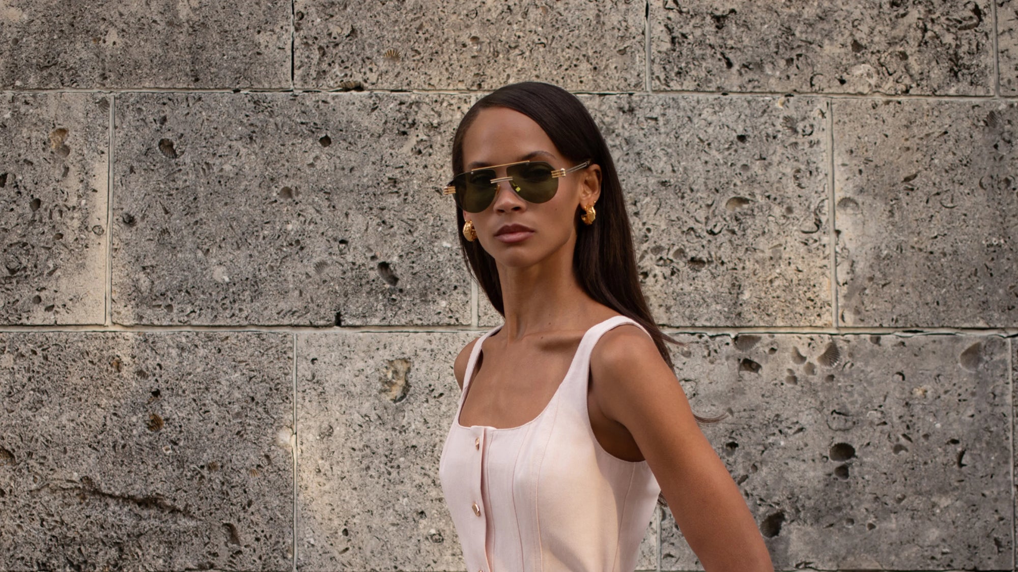 Woman wearing sunglasses and Karina Grimaldi white top against a stone wall.
