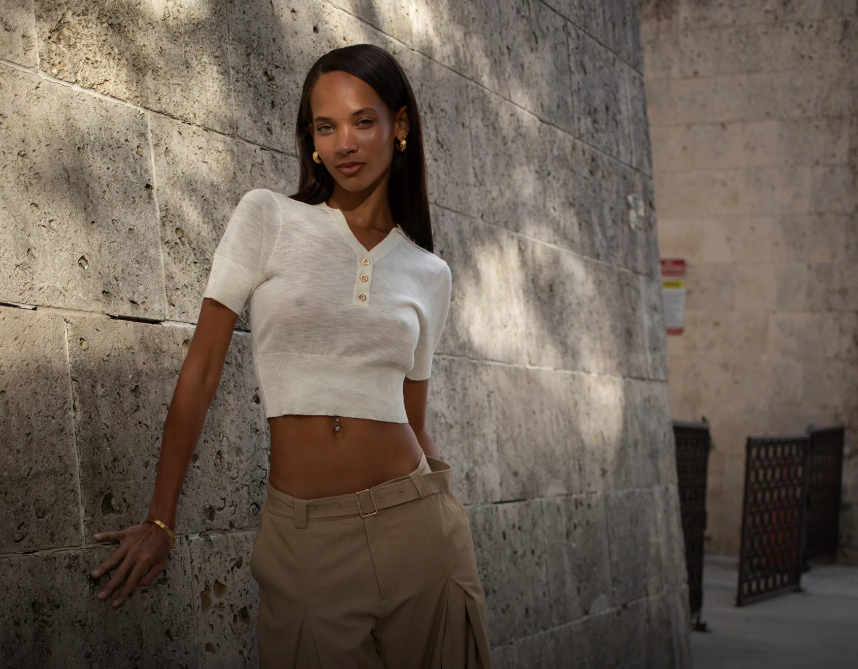 Woman in a white top and beige pants leaning against a stone wall.