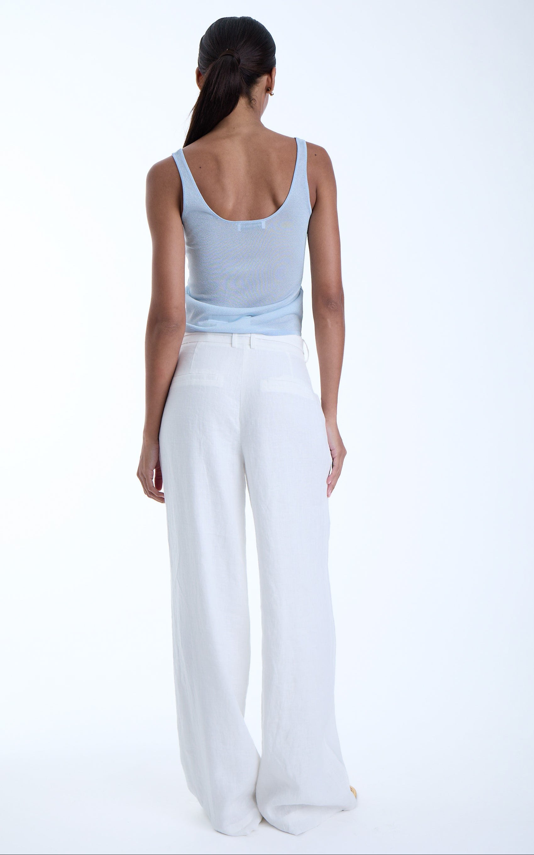 Woman wearing a light blue tank top and white pants on a white background