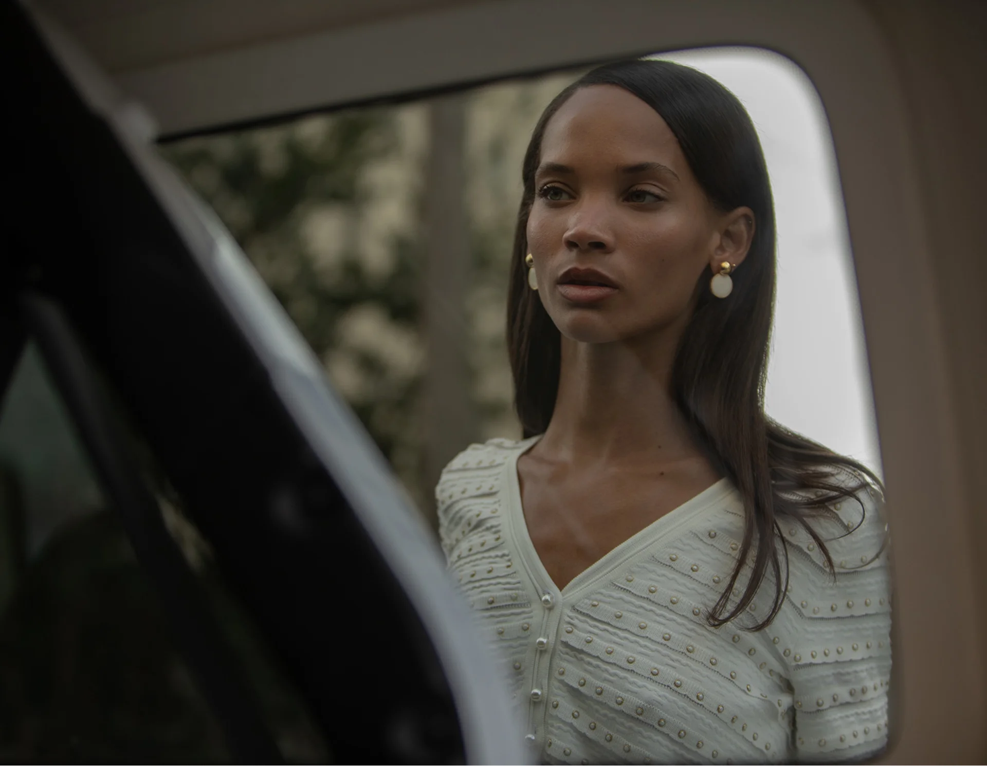 Woman looking out of a car window with a blurred background Wearing Karina Grimaldi White Dress