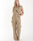 Woman wearing a beige Sola Trench Vest sleeveless jacket and pants on a white background
