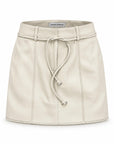 Karina Grimaldi Brair Vegan Leather Skirt in stone, front view, mini length with a self tie belt and punched trim at the hem and seams