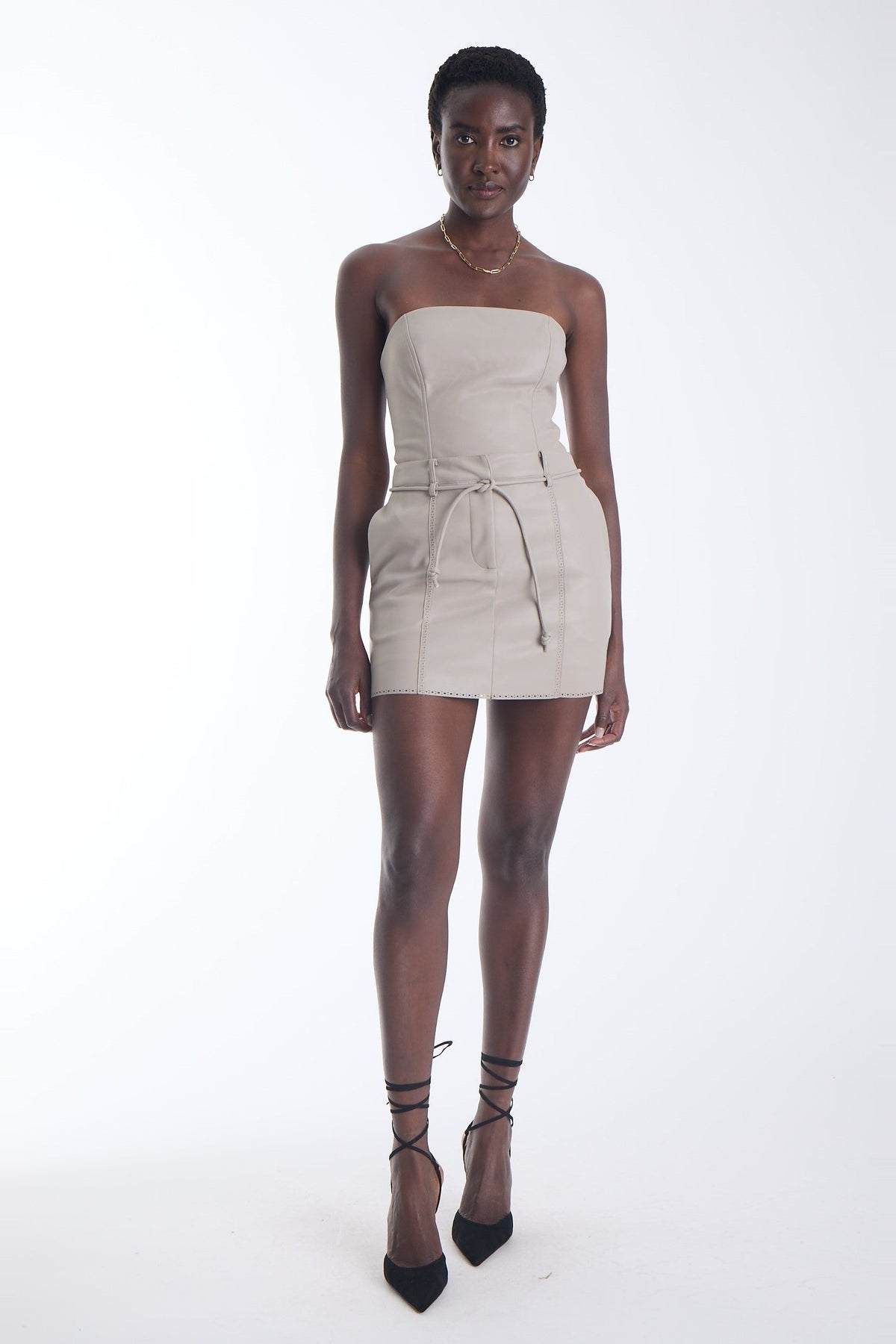 Karina Grimaldi Brair Vegan Leather Skirt in stone, front view on model, mini length with a tie belt and perforated trim at the hem