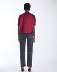 Karina Grimaldi Thea Blouse in mulberry satin, back view on model, plain back with short wide sleeves, worn with jeans