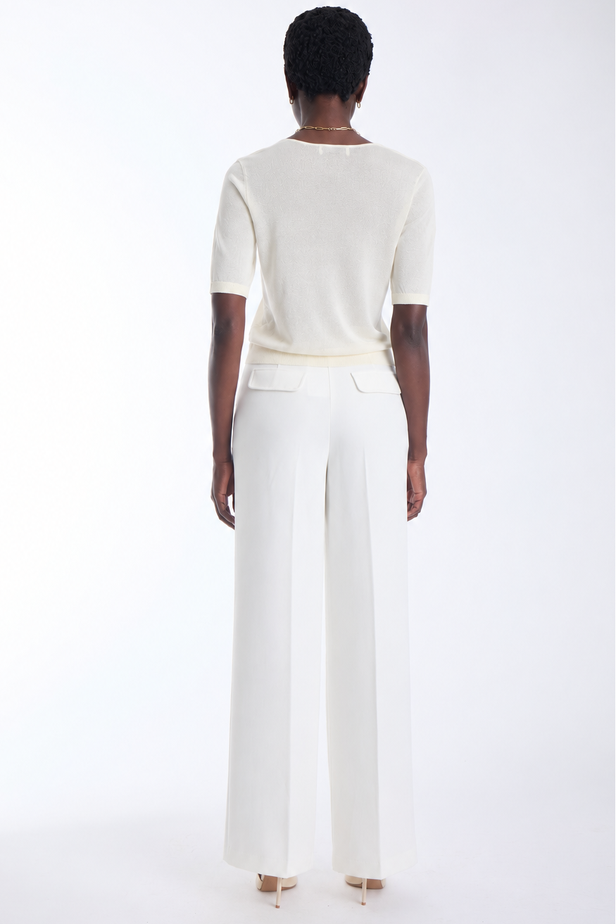 A model viewed from the back wearing a cream short-sleeve knit top and matching cream wide-leg trousers against a plain white studio background.
